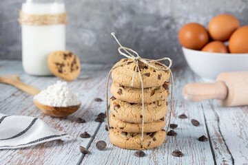 Stack of biscuits tied with string. Typical American Cookie with chocolate chips. Bottom decorated with milk bottle, rolling pin, eggs, chocolate chips and flour.