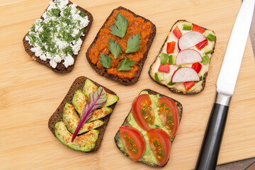 Various vegan, vegetarian healthy toasts on wooden board on kitchen with different vegetables and greens, top view