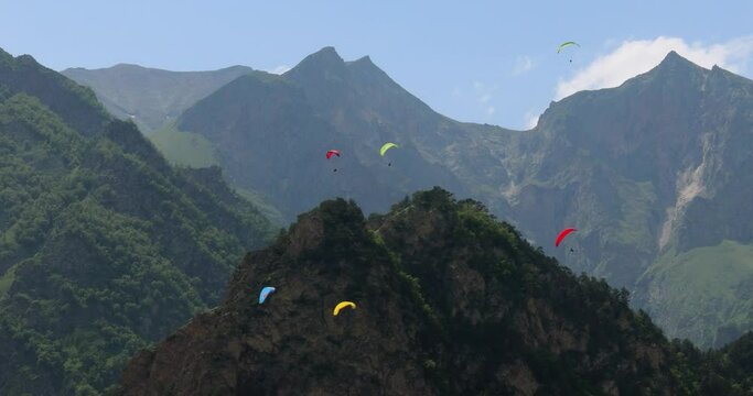 Paragliding pilots fly paragliders among clouds and green mountains.