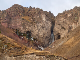 Steep rocky area with a waterfall flowing down from the river between the rocks. Mighty mountains of the Caucasus
