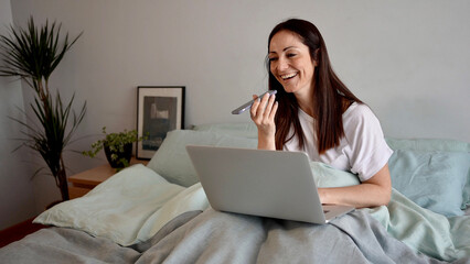 A happy woman using speakerphone for conversation with her friend while working from home. Businesswoman using audio application to send voice message.