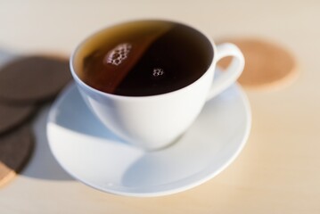 Black tea in a cup with a saucer lying on a wooden table. Weak, breakfast ritual. Detail focused on the level of herbal tea. Morning cleansing.