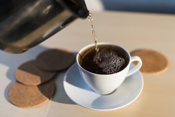 Preparation of black tea for breakfast. A kettle, a cup of tea, water. Underlay table with imitation wood.