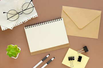 Blank notepad page on brown background and an envelope. Top view, office supplies. Mockup, copy space, diary concept, top view. Flat lay, top view.