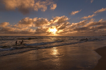 personas bañandose en la playa en la puesta de sol