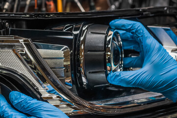 Car headlight in repair close-up. An auto mechanic wearing gloves installs the lens into the...