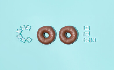 Chocolate glazed donuts and ice cubes in creative cool text against pastel blue background, Summer trendy layout. 