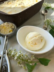 Ice cream with mango slices and an ice cream spoon on the table. Spring mood. Ice cream balls on the table among the white flowers on the table.