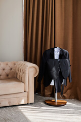 The groom's wedding suit on a hanger. A room with a sofa