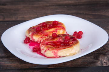 fried cheesecakes with red cherry syrup and cranberries, on a white plate