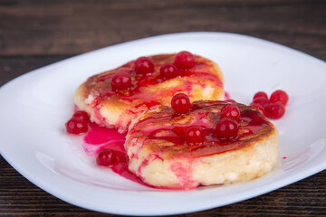 fried cheesecakes with red cherry syrup and cranberries, on a white plate