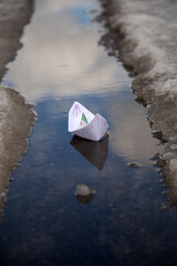a painted paper boat floats in a puddle of melted snow