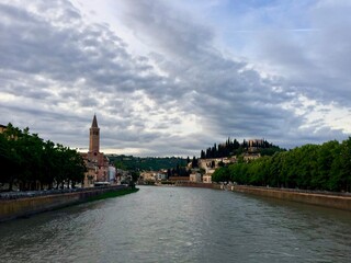 Verona, Italy. Town view from Nuovo del Popolo bridge over Adige river. Sunset, Bell tower of Santa Anastasia church. Cloudy sky. Green trees