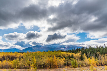 Cloudy afternoon views in northern Canada during autumn season with magnificent clouds covring the blue sky above mountain tops. 