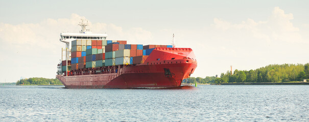 Container ship (168 meters length) leaving port terminal at sunset. Baltic sea. Freight...