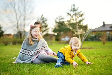 Fototapeta premium Big sister and her toddler brother having fun outdoors. Young girl playing with baby boy on spring day. Children with large age gap.