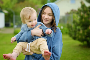 Fototapeta premium Cute big sister cuddling with her toddler brother. Adorable teenage girl holding baby boy. Children with large age gap. Big age difference between siblings.