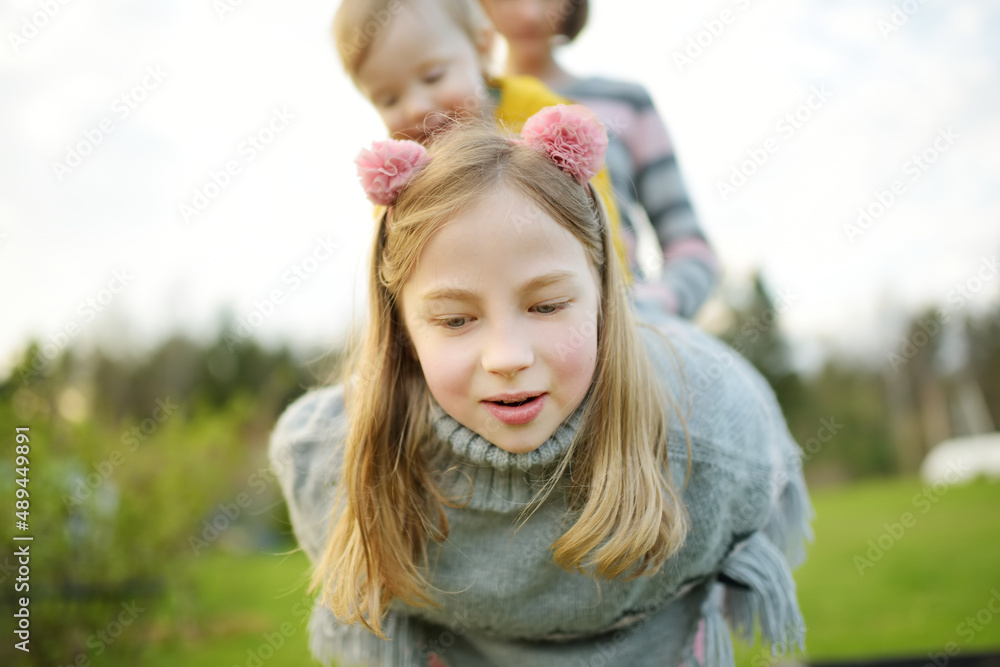 Poster Two big sisters and their toddler brother having fun outdoors. Two young girls holding baby boy on summer day. Children with large age gap. Big age difference between siblings.