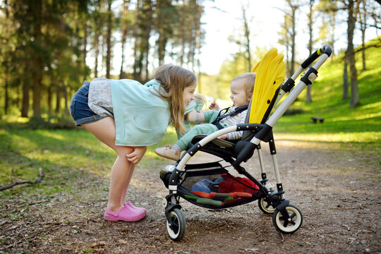 Older sister and her toddler brother sitting in a stroller outdoors. Infant kid in pushchair. Summer walks with kids.