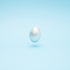 Easter creative layout made with silver Easter egg levitating on a pastel blue background. Minimal holiday still life concept.