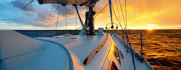 White yacht sailing in an open sea at sunset. A view from the deck to the bow, mast, sails. Epic...