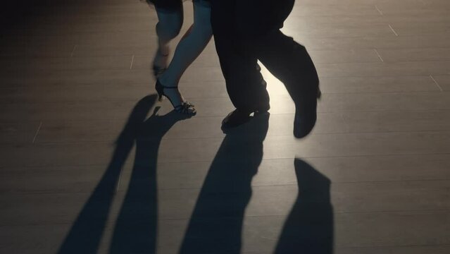 Couple legs doing latin dance steps on floor. Unknown partners dancing choreography Argentine tango. Man and woman dance in dark with backlight. Close up. Slow motion ready, 4K at 59.94fps.