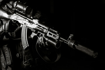 Man in black uniform aiming with silenced Kalashnikov assault rifle on black background
