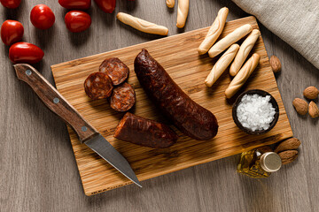 aerial shot of cherry tomatoes and chorizo o sausage on a board with bread and salt. Knife and olive oil