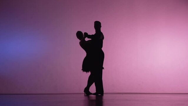 Elements of Argentine tango performed by pair of dancers. Silhouettes of man and woman dancing latin dance choreography in studio with blue pink background. Slow motion ready, 4K at 59.94fps.