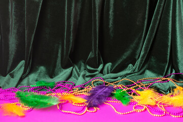 Festive carnival background, green velvet curtain colorful feather beads necklace for Mardi Gras 
