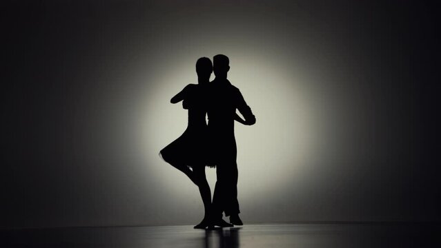 Passionate tango choreography elements performed by pair of ballroom dancers. Black silhouettes of man and woman moving on gray background with backlight. Slow motion ready, 4K at 59.94fps.
