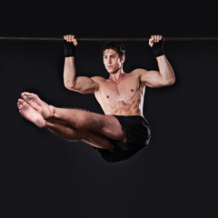 Power and endurance. Studio shot of a young man doing pull-ups from a bar.