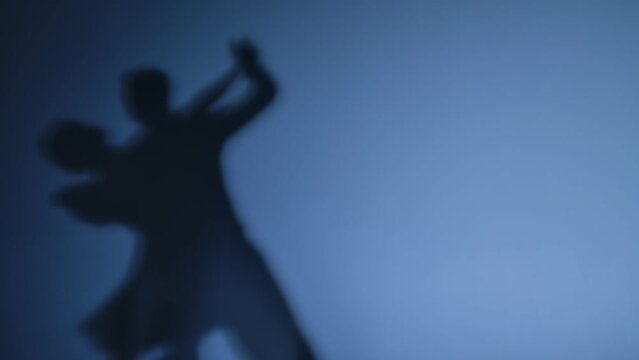 Dancing shadows of ballroom dancers performing Argentine tango on a blue studio background. Man and woman practice elements of Latin choreography. Close up. Slow motion ready, 4K at 59.94fps.