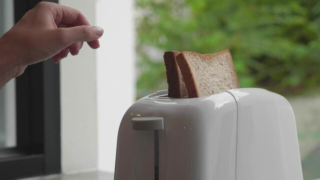 Two pieces of bread in toaster slots. Two larger hands take out pieces of bread. Two hands take out pieces of bread close-up