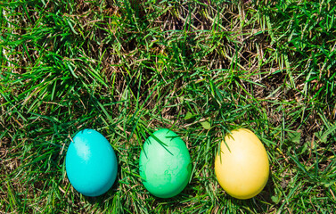 Top view of three multicolored Easter eggs lined up against a background of grass. Flat style, Easter holiday concept.