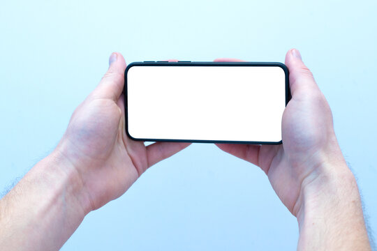des mains tiennent un t&eacute;l&eacute;phone &agrave; l'horizontale afin de regarder un film ou une vid&eacute;o ou bien de jouer. L'&eacute;cran du smartphone est blanc. Vous pouvez placer votre image. Isol&eacute; sur fond bleu