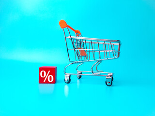 Shopping chart and wooden block with persentage symbol on blue background.