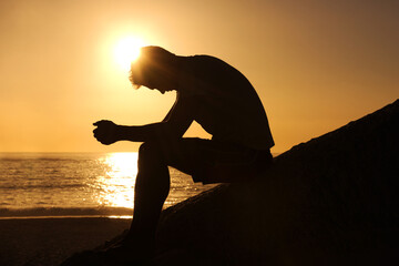Contemplating the meaning of life. Silhouette of a man sitting by the ocean and contemplating while...