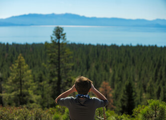 Boy looks through binoculars at forest and lake