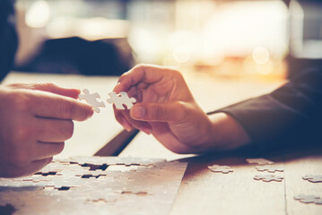 Group of Business people hands are holding and conecting jigsaw puzzle on desk and solving puzzle together at meeting in the office. Assembling, Solutions, Success and Strategy concept.Business  - obrazy, fototapety, plakaty