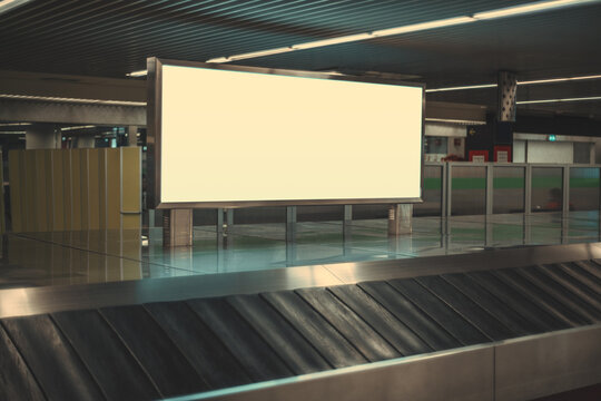 A Blank Advertising Poster In An International Airport Near An Empty Moving Luggage Belt. Baggage Claim Area With A Long Horizontal Advertisement Banner Or A Digital Informational Billboard Mockup