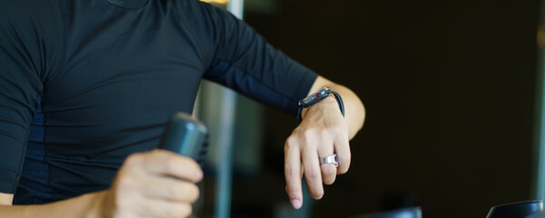 Happy sportsman using a smartwatch or exercise tracker on his wrist to track an exercise, sport man touching a smartwatch screen while exercising on a elliptical exercise machine. Serious workout.