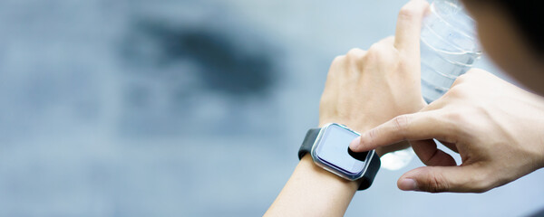 Active Asian young sportsman using a smartwatch or smart fitness band to track his outdoor workout and activities, man reviewing an exercise and health information after finished outdoor workout.