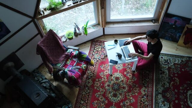 Young man working and relaxing with laptop in vintage style geo dome. Vintage carpet on the floor, rocking chair, paintings on the walls