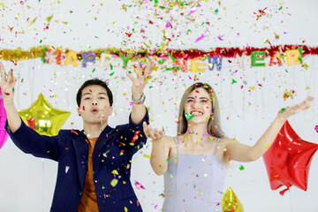 Millennial young lover couple Asian husband in casual suit and beautiful wife smiling holding red wrapped present gift box celebrating happy new year party in full decorated room with star balloons