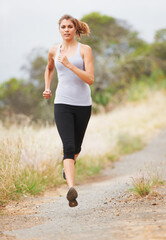 Running for fitness. A young woman running on a dirt road.