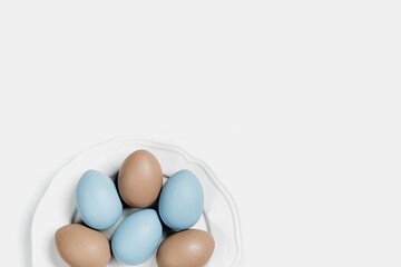 Dyed Easter eggs pastel colors blue, beige on round white plate. Happy Easter holiday concept, celebration food, decorated chicken egg, neutral trendy colored card. Top view table