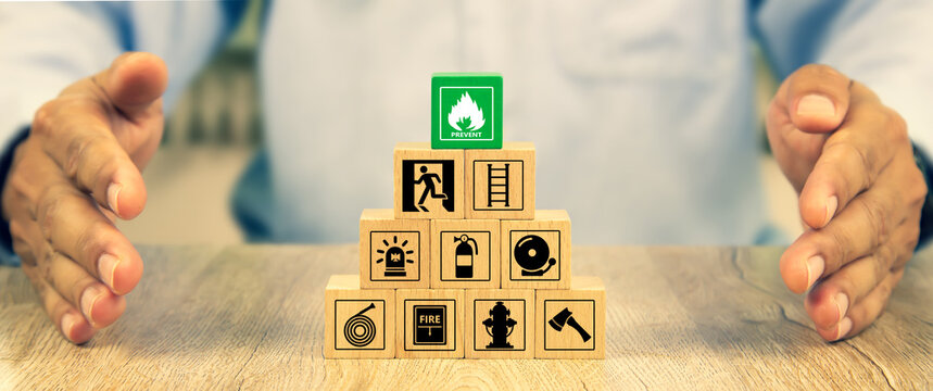 Cube wooden toy block stack in pyramid with hand protect with fire icon and door exit sing or fire escape with prevent and fire extinguisher and emergency protection symbol for safety and rescue.