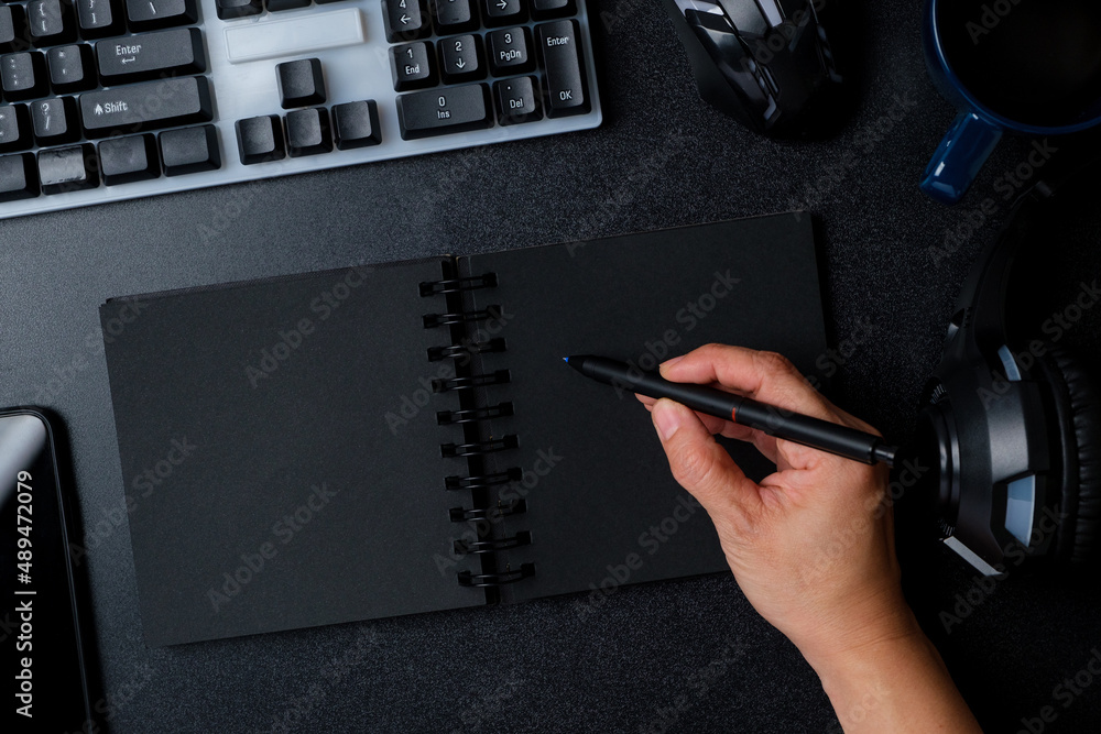 Poster top view hand writing on notebook working on desk with keyboard headphone on black table background
