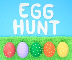 Egg hunt letters on blue background and coloured eggs with polka dot on a green grass